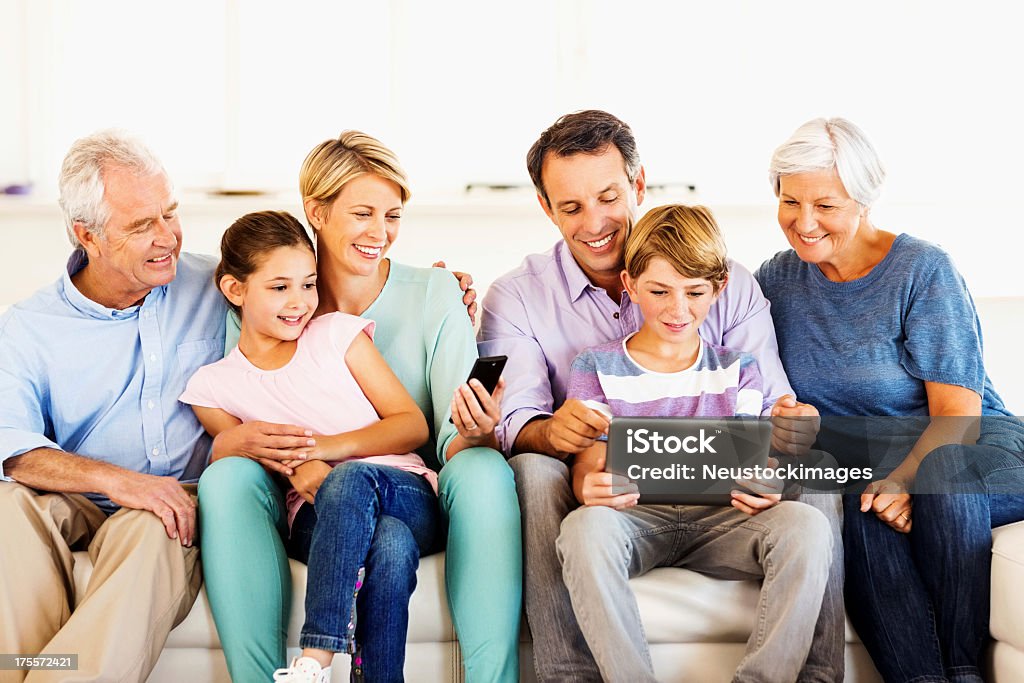 Three generation family smiling while using smart phone and digital tablet at home. Horizontal shot.